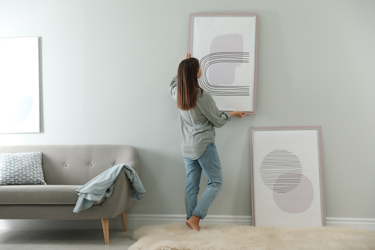 Giovane donna appende quadri nel soggiorno di casa