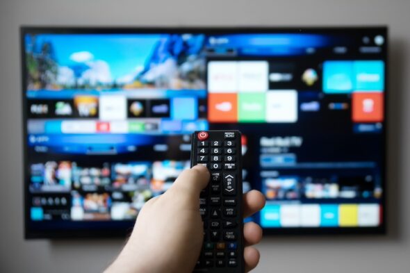 una persona con telecomando in mano con tv in sottofondo