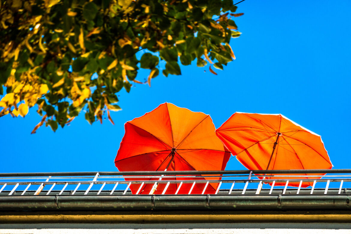 Ombrelloni arancioni sul balcone, con albero verde e cielo azzurro