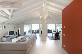 Interno di una casa un salotto con travi a vista, un divano e una parete rossa